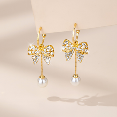 Gold crystal bow pearl drop dangle earrings on beige background
