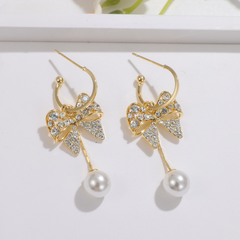 Gold rhinestone bow pearl drop earrings flat lay on white background