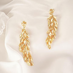 Pair of long gold leaf tassel drop earrings on white satin fabric
