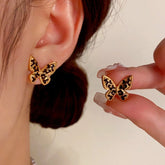 Black and gold leopard print butterfly stud earrings, one worn, one held by hand