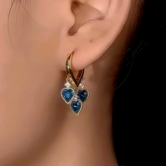 Model showcasing the dangle and style of the 14K Gold-Plated Blue Crystal Heart Tassel Earrings