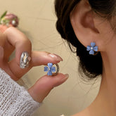 Dainty blue four-leaf clover earrings, held in hand and worn on ear