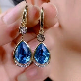 Pair of gold blue teardrop crystal drop earrings, closeup held in hand