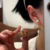 Hand holding gold pearl bow front-back drop earring beside ear wearing matching earring