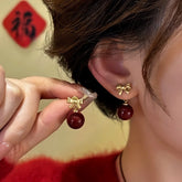 Gold bow dark red bead dangle earrings: one worn on ear, one held in hand