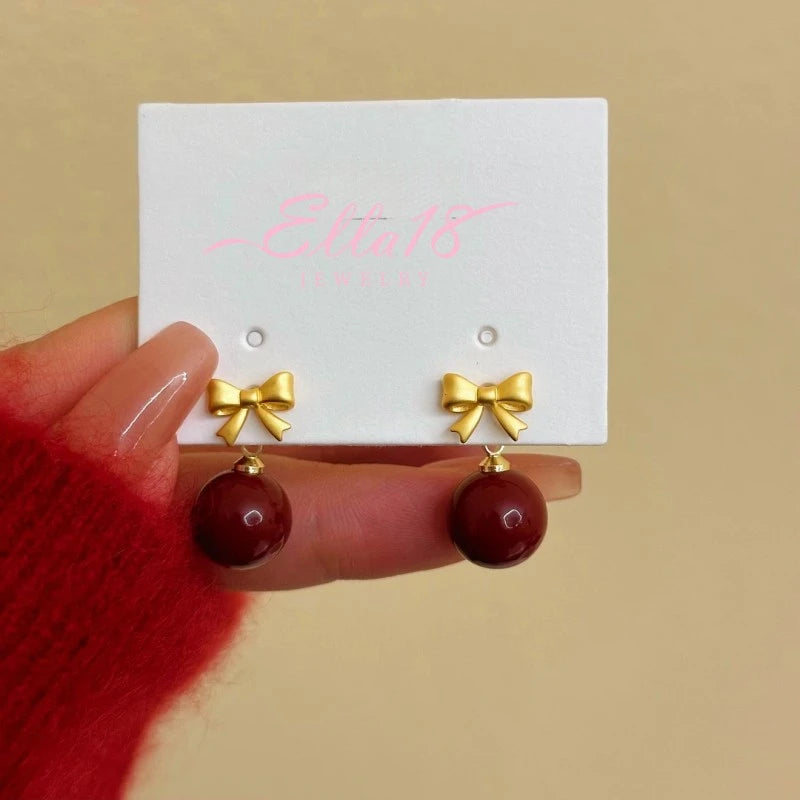 Angled view of the 14K Gold-Plated Bow Red Bead Earrings