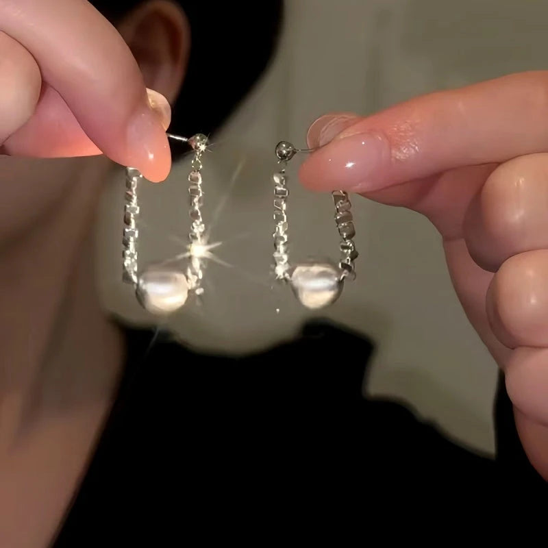 Pair of women's silver sparkly chain pearl drop earrings held between fingers