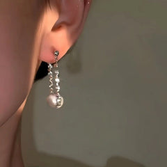 Women's shimmering silver pearl dangle earring on ear, warm light closeup