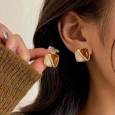 Gold amber white rounded square stud earrings: one worn on ear, one held in hand