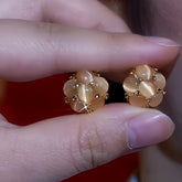 Pair of champagne cat's eye floral stud earrings held by fingertips