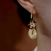Gold mesh teardrop dangle hoop earring with brown crystals worn on ear