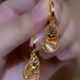 Pair of gold teardrop dangle earrings held in hand, close-up detail