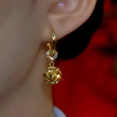 Close-up of sparkling gold crystal ball drop huggie hoop earring worn on woman's ear