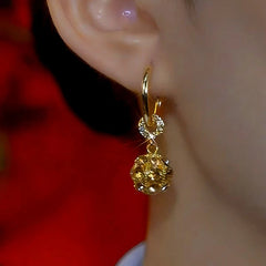 Side view of sparkling gold crystal ball drop huggie hoop earring worn on woman's ear