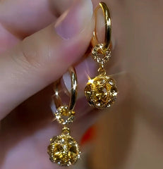 Pair of women's sparkling gold crystal ball drop huggie hoop earrings held in hand