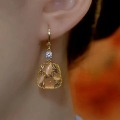 Side angle close up of gold square cat eye dangle earring on woman's ear