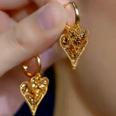 Pair of gold textured double heart dangle hoop earrings held between fingers
