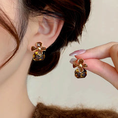Women's brown flower amber crystal drop earring pair, one worn, one held in hand