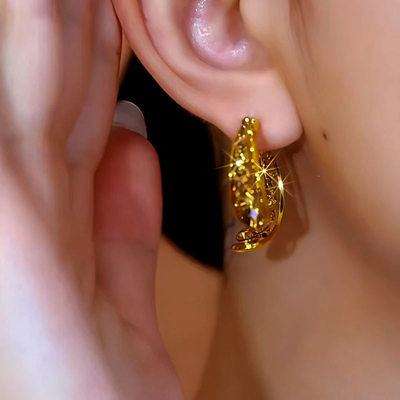 Sparkly carved gold hoop earring worn on woman's ear, closeup