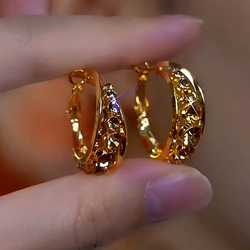 Pair of textured gold huggie hoop earrings, close-up held between fingers