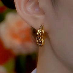 Gold textured huggie hoop earring worn on ear, side view with floral bokeh