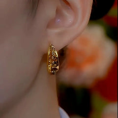 Carved gold huggie hoop earring worn on ear, front angle with soft floral background