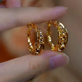 Close-up of textured gold huggie hoop earrings held between fingers