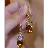 Pair of women's gold amber teardrop crystal drop earrings with leaf accents held in hand