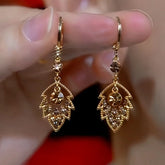 Gold champagne crystal leaf drop hoop earrings held between fingers