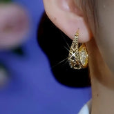 Gold teardrop crystal hoop earring worn on ear close-up