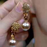 Hand holding pair of gold rhinestone leaf champagne pearl clip-on drop earrings