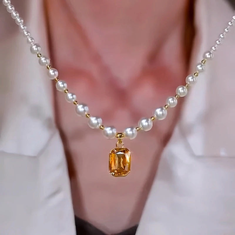 White pearl necklace with yellow emerald-cut gem pendant worn with white blazer