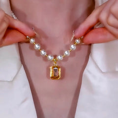 Hands adjusting white pearl necklace, showing back of gold gem pendant