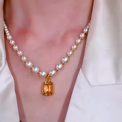 White pearl beaded necklace with yellow gem pendant worn with white collared shirt