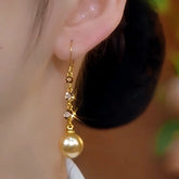 Close-up of a gold pearl drop earring with crystal accents worn on a woman's ear