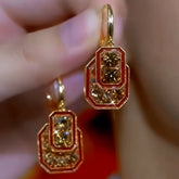 Pair of gold red enamel champagne crystal geometric drop earrings held in hand