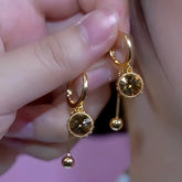 Pair of gold amber crystal drop hoop earrings held in hand