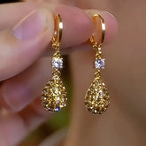 Pair of gold pavé teardrop dangle huggie hoop earrings with cubic zirconia, held by fingers