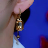 Gold rectangular champagne crystal drop earring worn on woman's ear, blue background