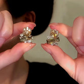 Pair of women's geometric champagne crystal stud earrings held between fingers
