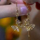 Gold crystal butterfly dangle earrings held between fingers