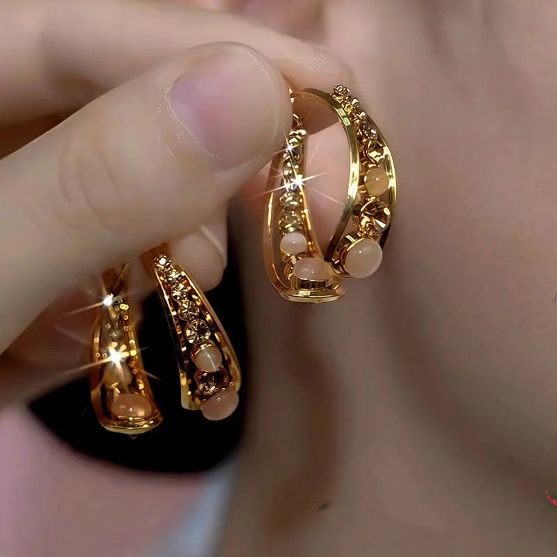 Pair of layered gold hoop earrings with opal beads and crystal accents held in hand