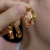 Pair of layered gold hoop earrings with opal beads and crystal accents held in hand