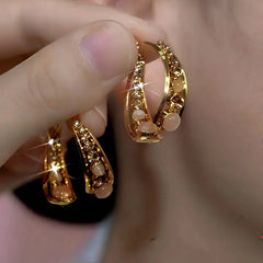 Pair of layered gold hoop earrings with opal beads and crystal accents held in hand