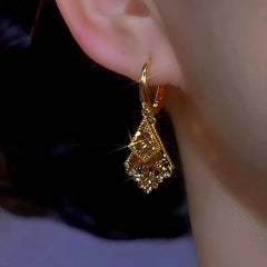 Gold layered geometric sparkly drop hoop earring worn on earlobe