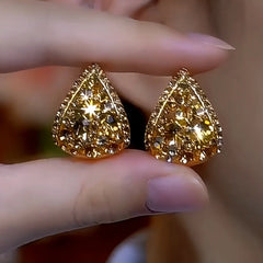 Pair of gold teardrop pave crystal stud earrings held between fingers