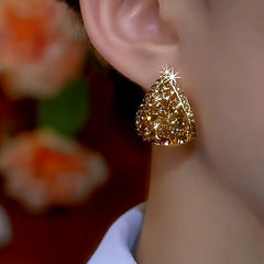 Gold teardrop pave stud earring worn on female ear, close-up
