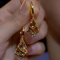 Hand holding pair of gold layered geometric sparkly drop hoop earrings