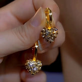 Pair of sparkling gold pave crystal heart drop hoop earrings held in hand