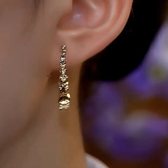 Faceted gold hoop earring worn on a person's earlobe
